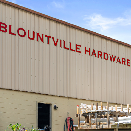 Tan metal building with red Blountville Hardware letters. Lower half features yellow-painted cinderblocks.