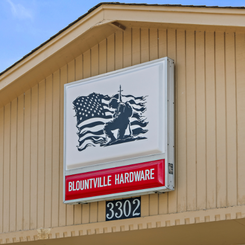 Soldier with a cross in front of a wavy black and white American flag. Below, Blountville Hardware in white text on a red background.