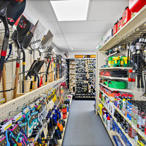 An aisle filled with shovels, hoses, WD-40, garden gloves, pitchforks, gas cans, and more.