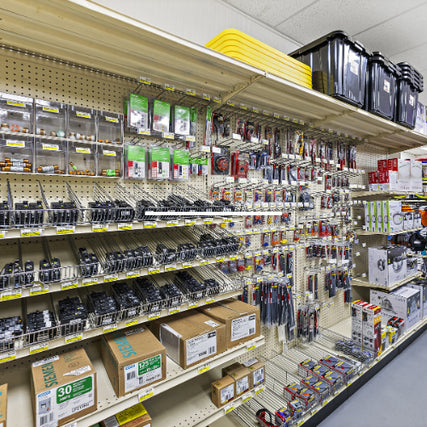 Electrical SuppliesA well-organized hardware store aisle featuring a variety of electrical supplies, including outlet covers, switches, circuit breakers, and wiring accessories. Shelves are stocked with neatly arranged packages and boxes of electrical components.